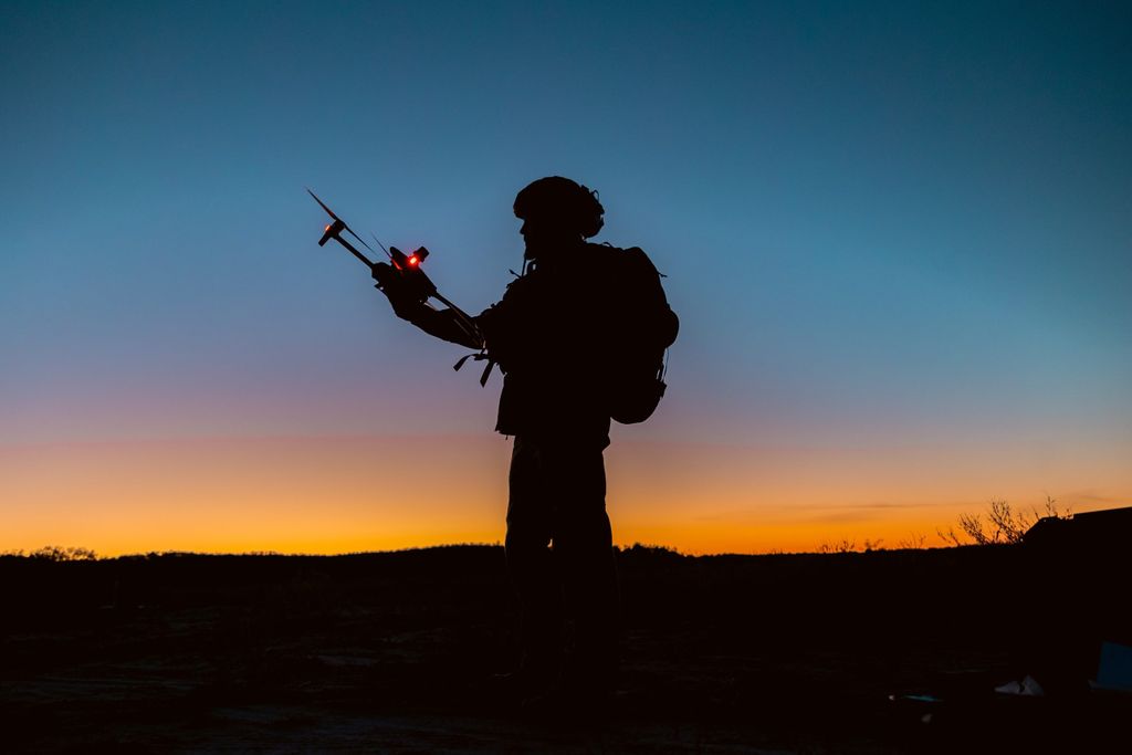 Silhouette of a soldier preparing to operate drone at dusk.
